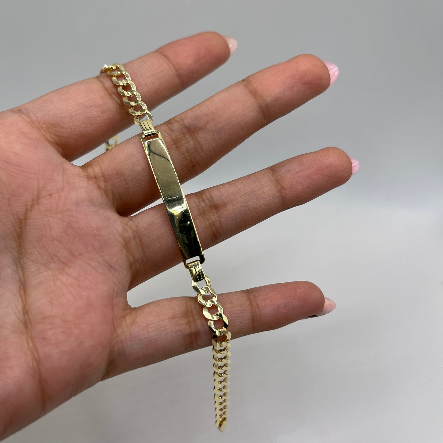 Gold chain bracelet on a hand against a plain background