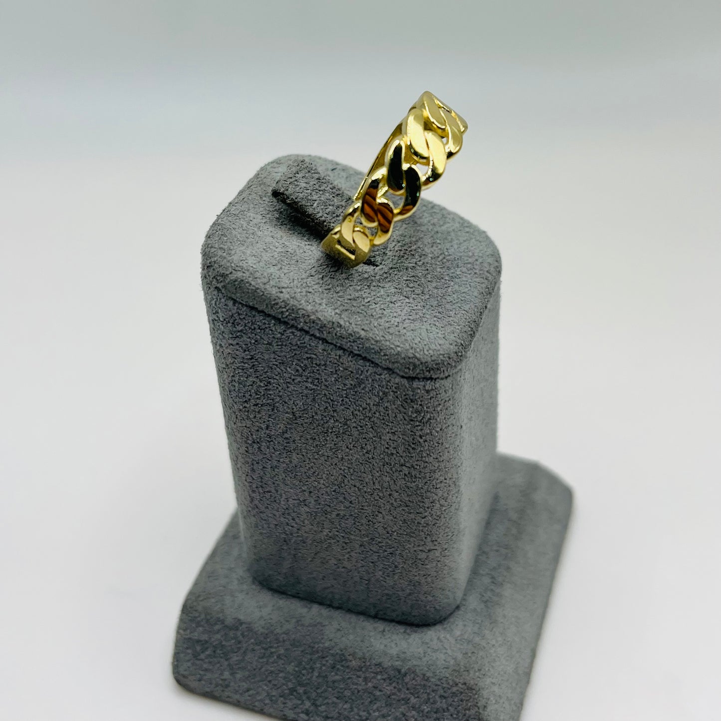 Gold chain ring on a gray jewelry display stand against a white background