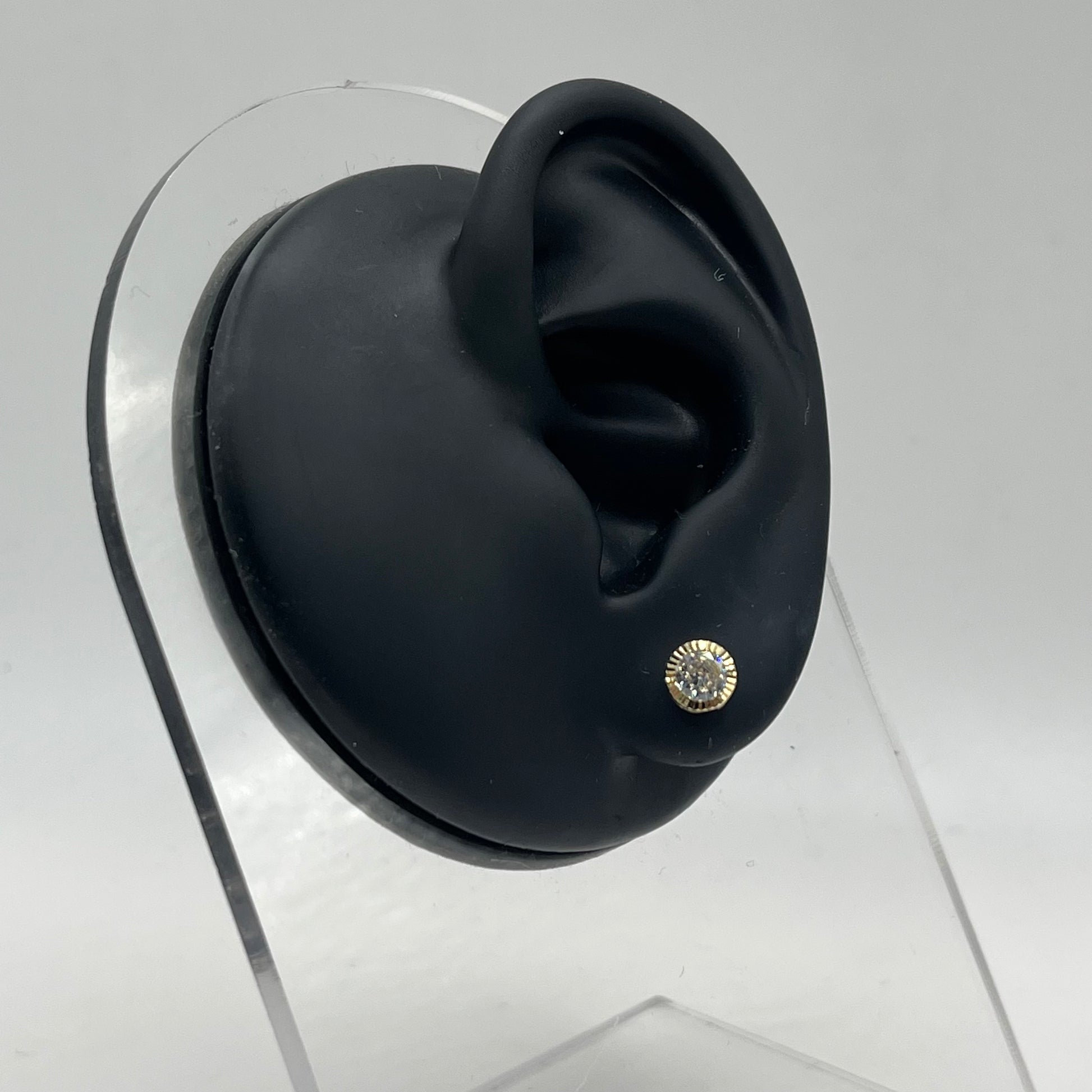 Black ear with a gold earring on a clear stand against a gray background
