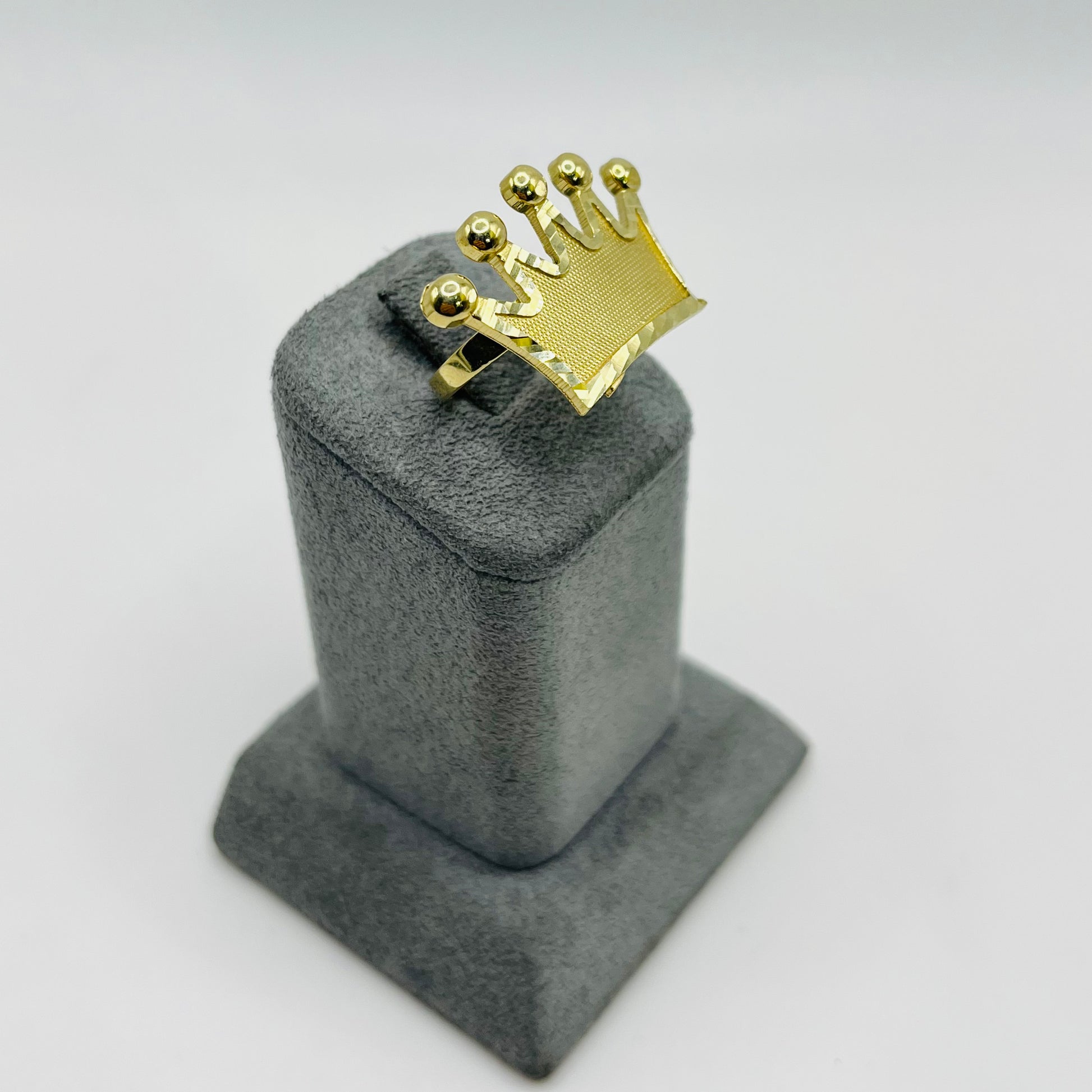 Gold ring with a crown design on a gray stand against a white background