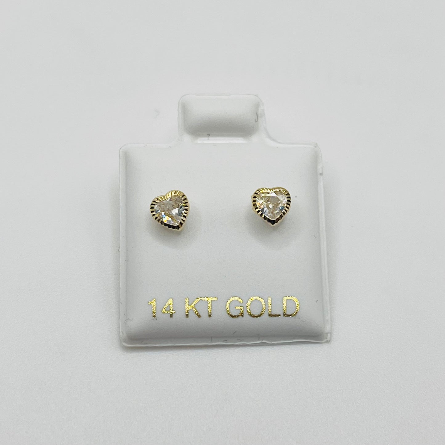 Heart-shaped gold earrings on a 14 KT Gold branded card against a light gray background