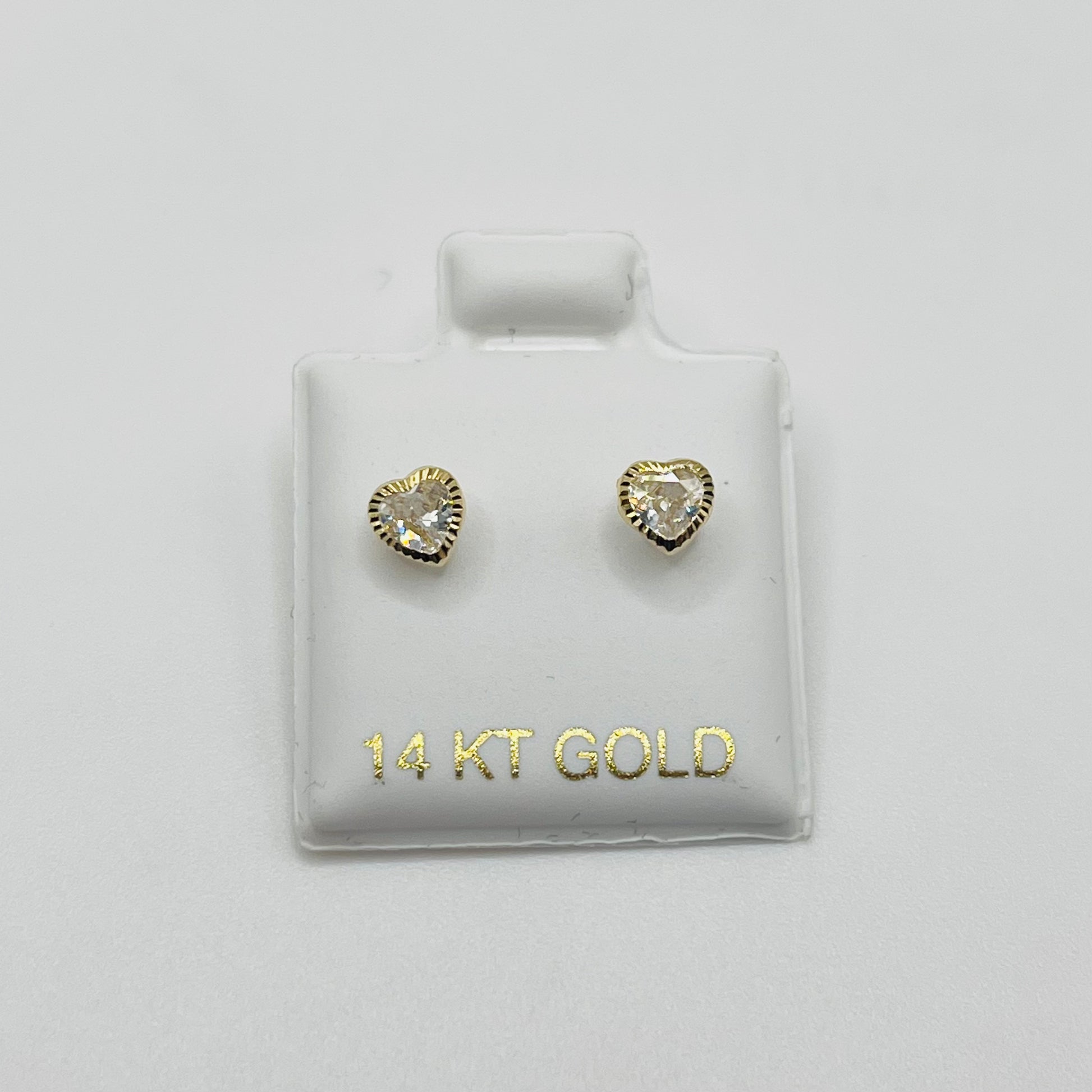 Heart-shaped gold earrings on a 14 KT Gold branded card against a light gray background