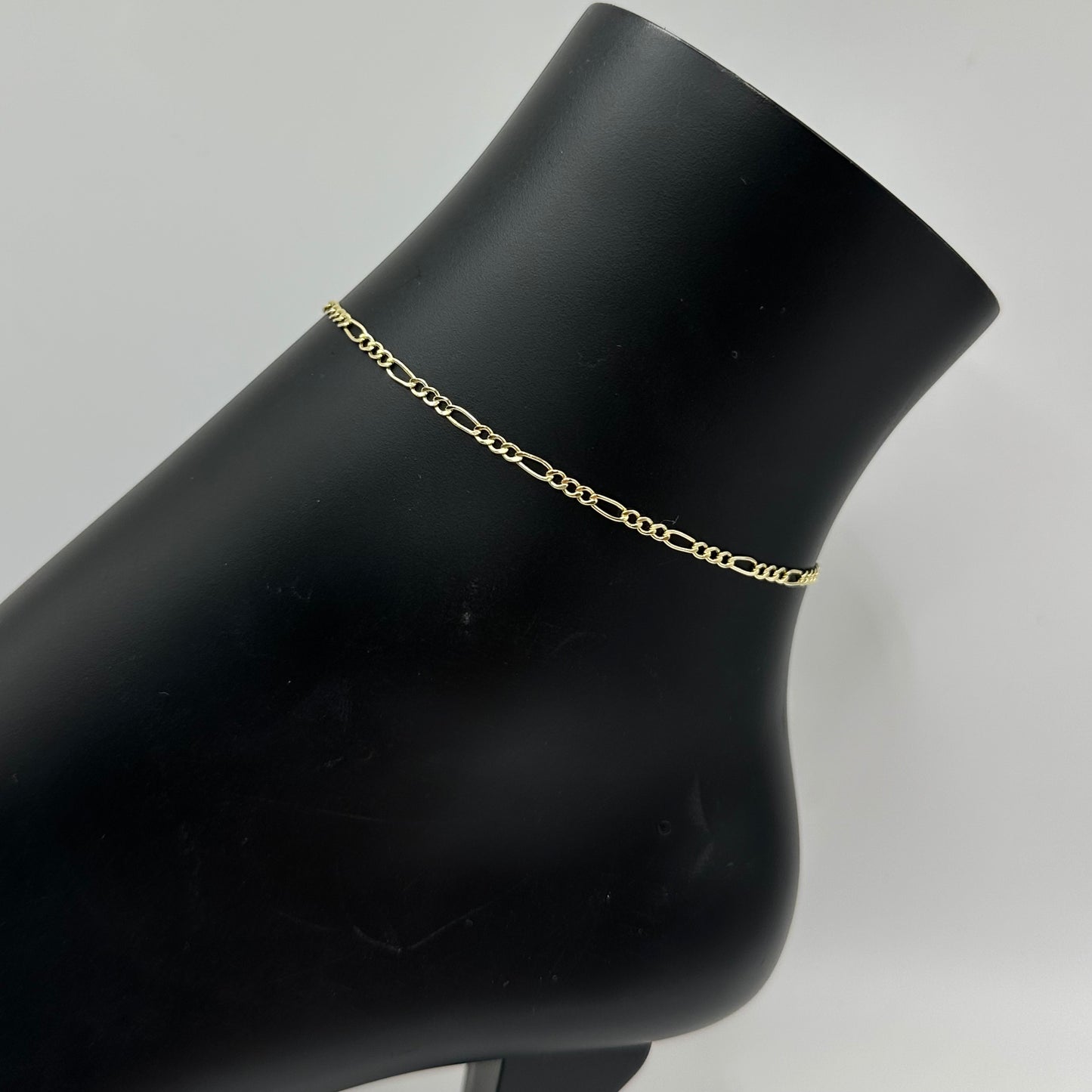 Gold chain bracelet on a black mannequin arm against a gray background