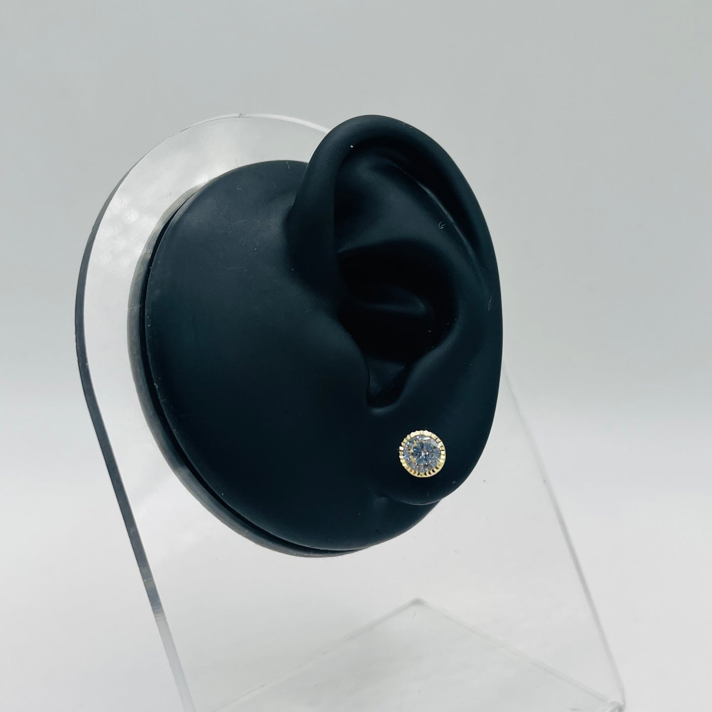 Black ear with a diamond-studded earring on a clear stand against a gray background