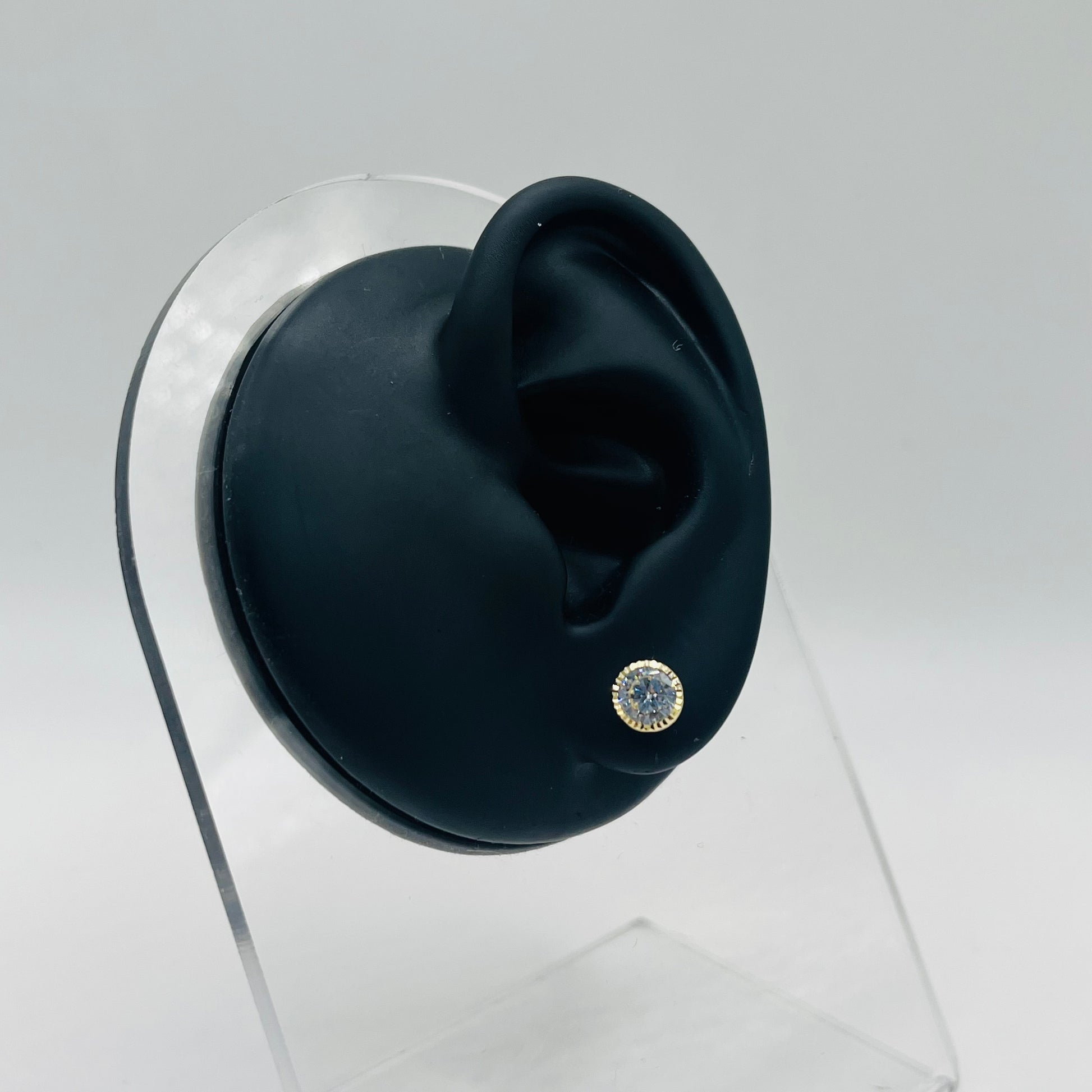 Black ear with a diamond-studded earring on a clear stand against a gray background