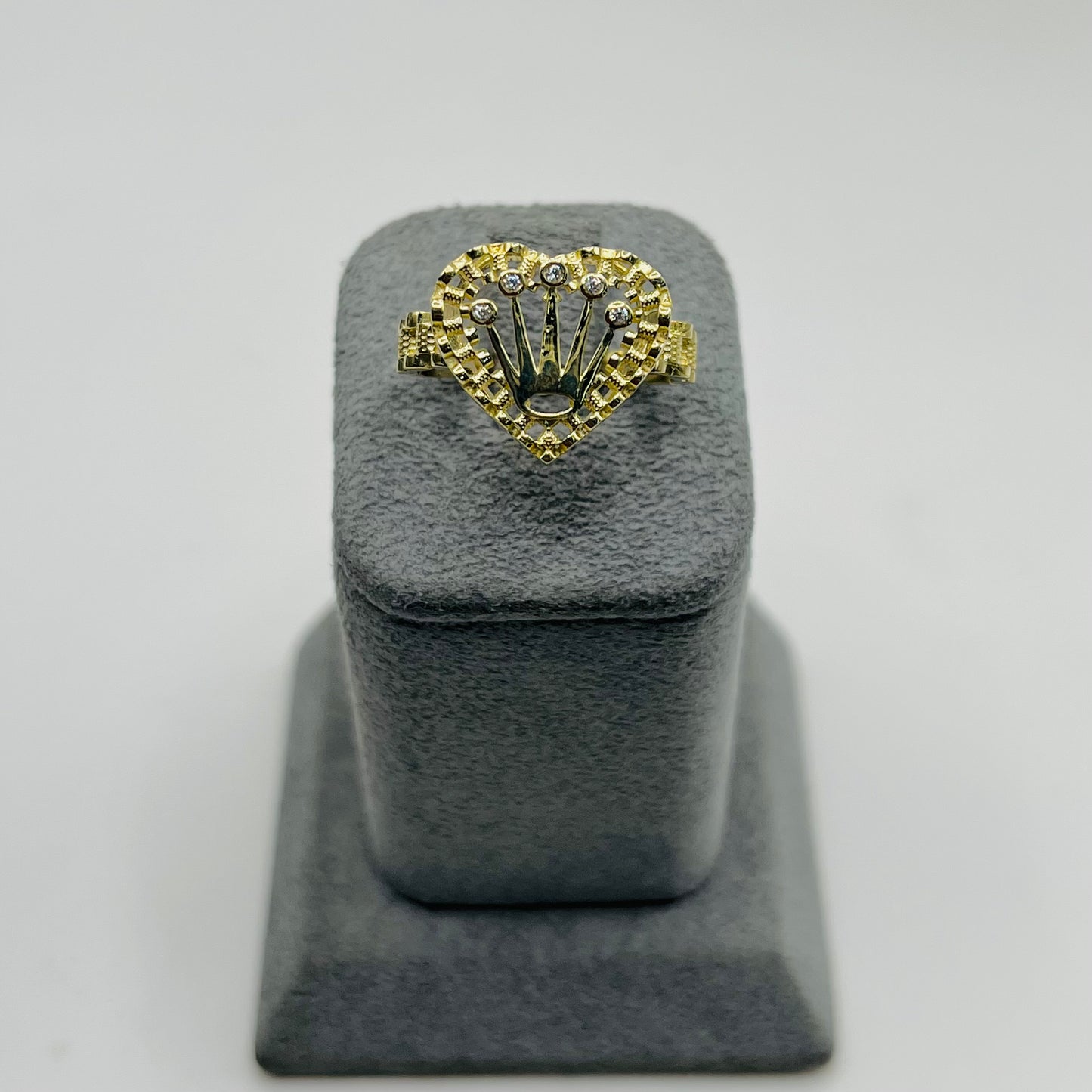 Gold ring with heart design on a gray stand against a light gray background
