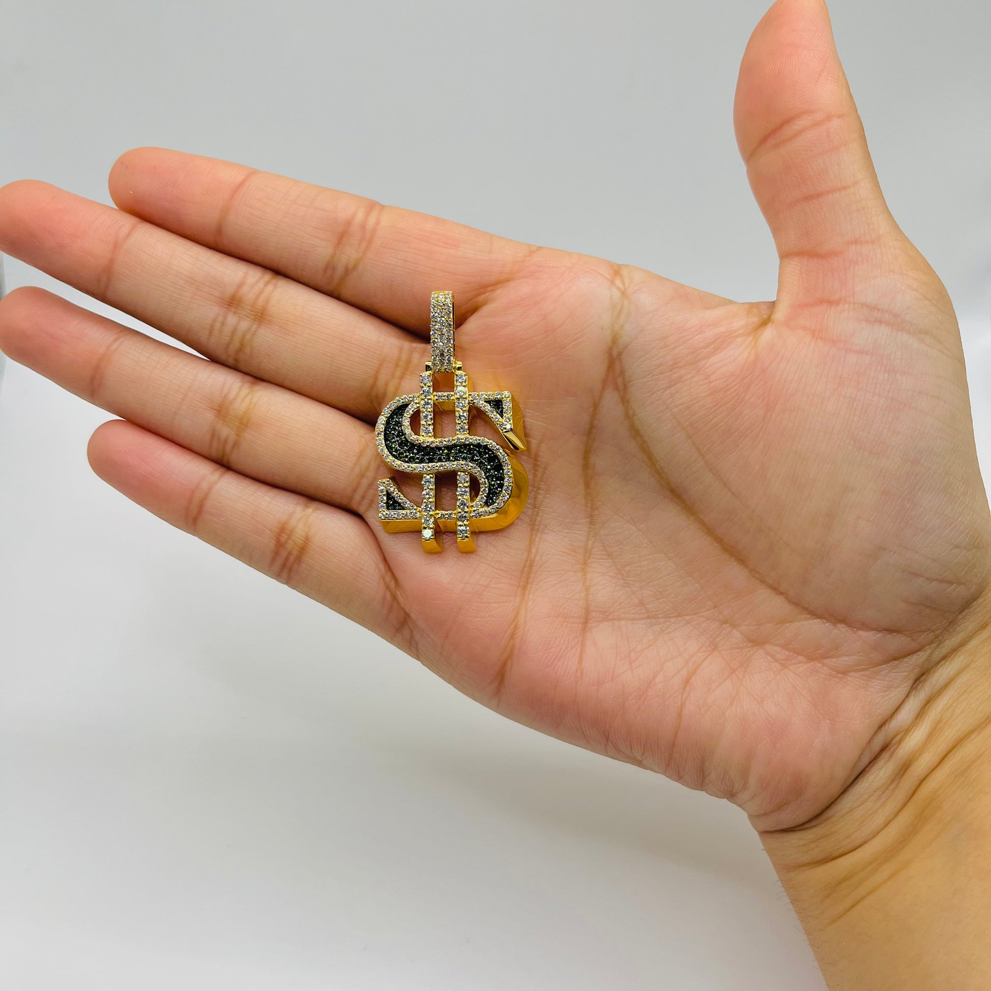 Gold and black dollar sign pendant held in a hand against a plain background