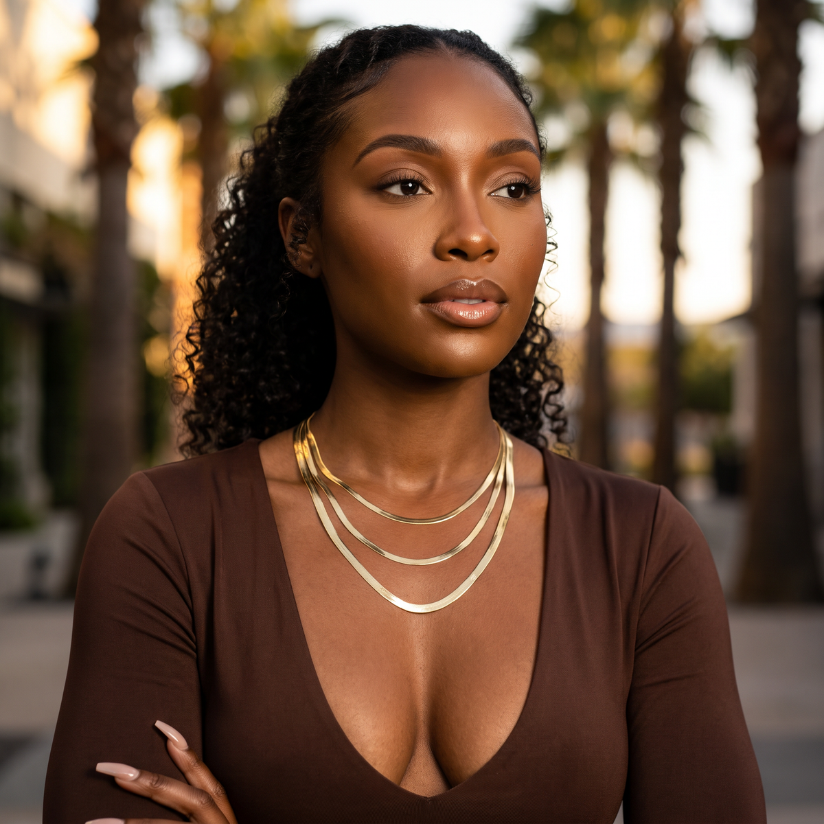 10k Gold Herringbone Chain on a woman walking and crossing her arms with palm trees in the background.