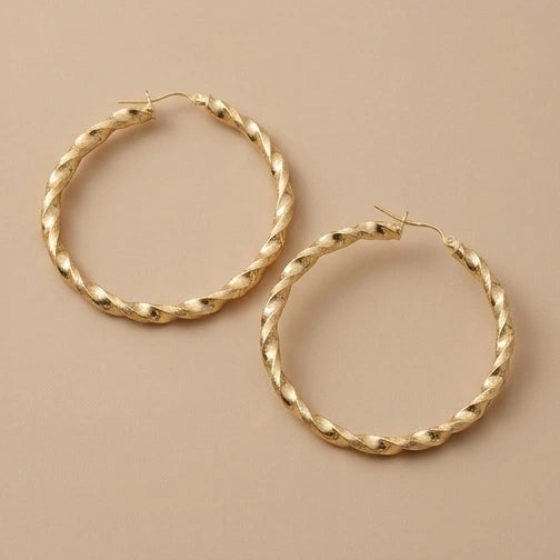 A pair of 10K Gold Twist Hoop Earrings with a twisted rope texture, displayed on a solid beige background.