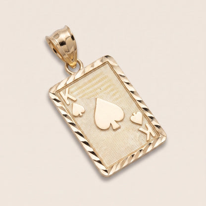 A 10K Gold King of Spades Charm designed like a playing card, featuring a textured center with raised spade suit symbols and a twisted rope-style border, shown on a light beige background.