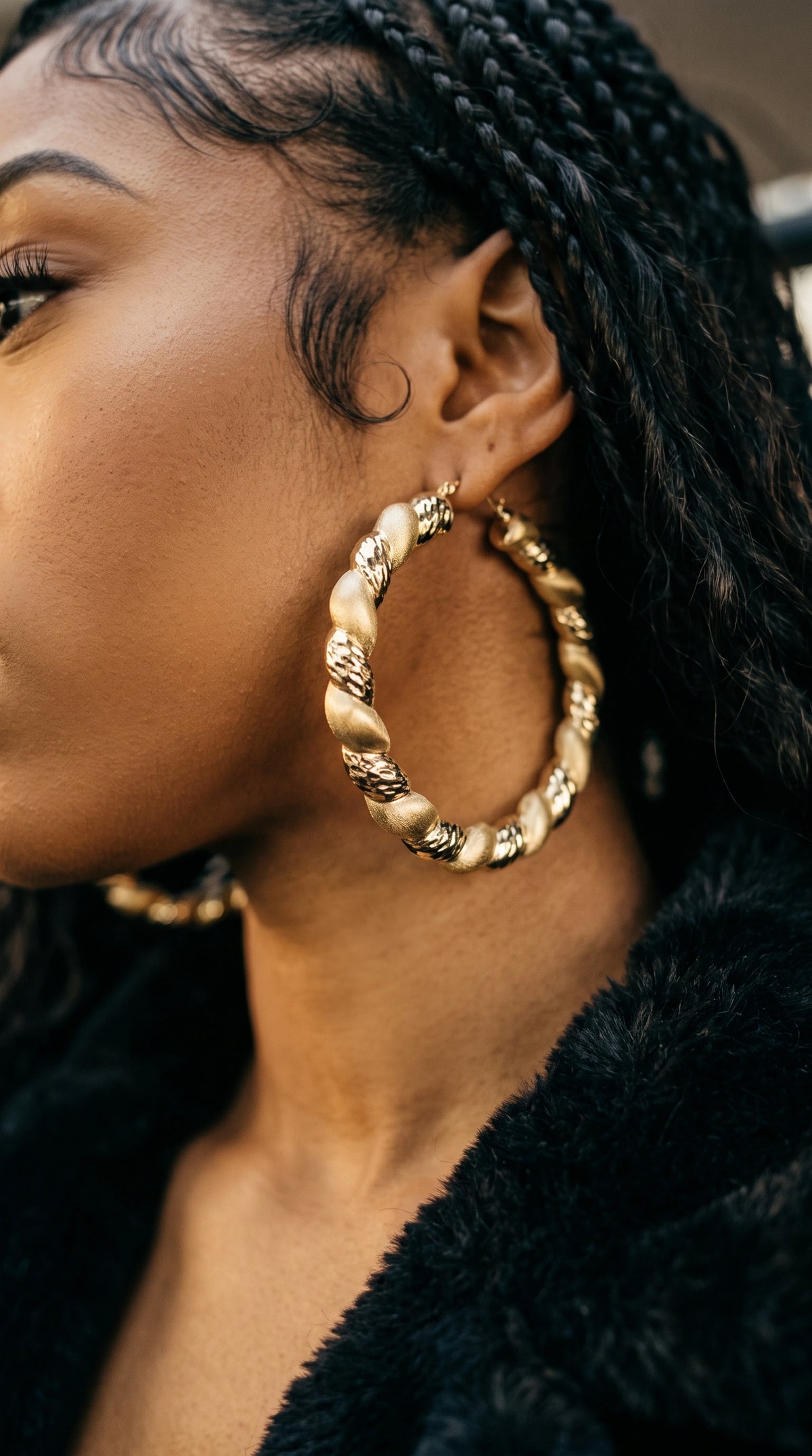 A close-up side profile of a woman wearing 10K Gold Matte and High Polish Hoop Earrings and a black faux-fur collar.