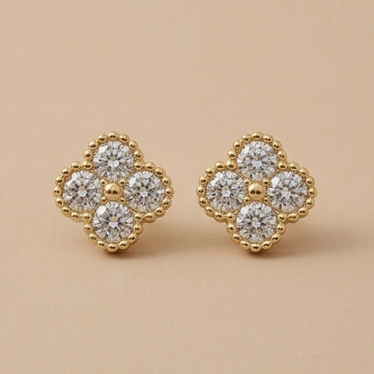 A pair of 10K Gold White Clover Earrings with a four-petal flower design, featuring clear round-cut cubic zirconia surrounded by a beaded gold border, set against a solid beige background.
