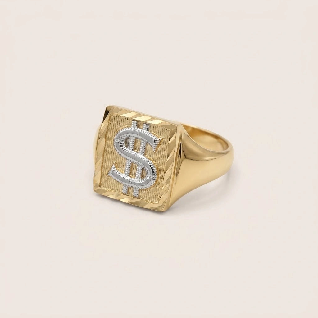A 10k Gold Two-Tone Dinero Ring featuring a textured square face with a silver dollar sign symbol inlaid on top, set against a plain light beige background.