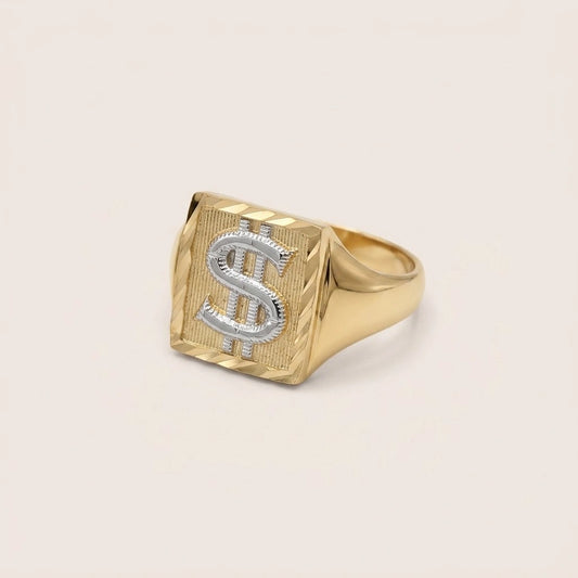A 10k Gold Two-Tone Dinero Ring featuring a textured square face with a silver dollar sign symbol inlaid on top, set against a plain light beige background.