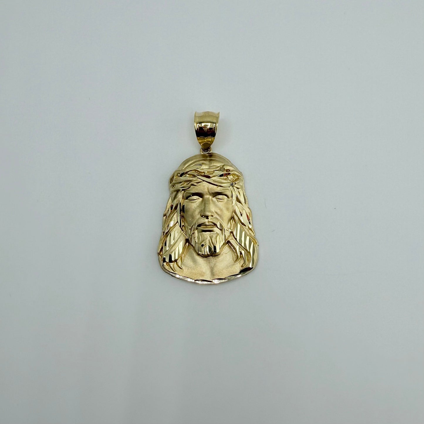 Gold pendant with a face design on a gray background