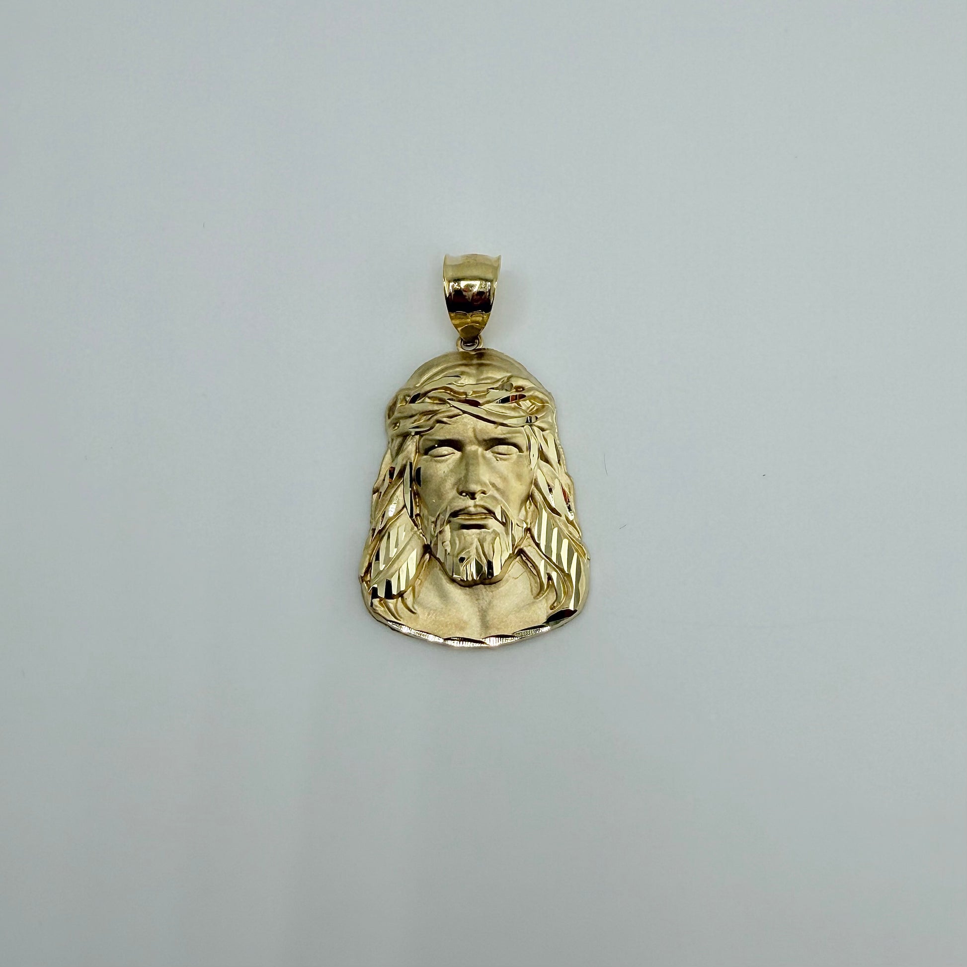 Gold pendant with a face design on a gray background