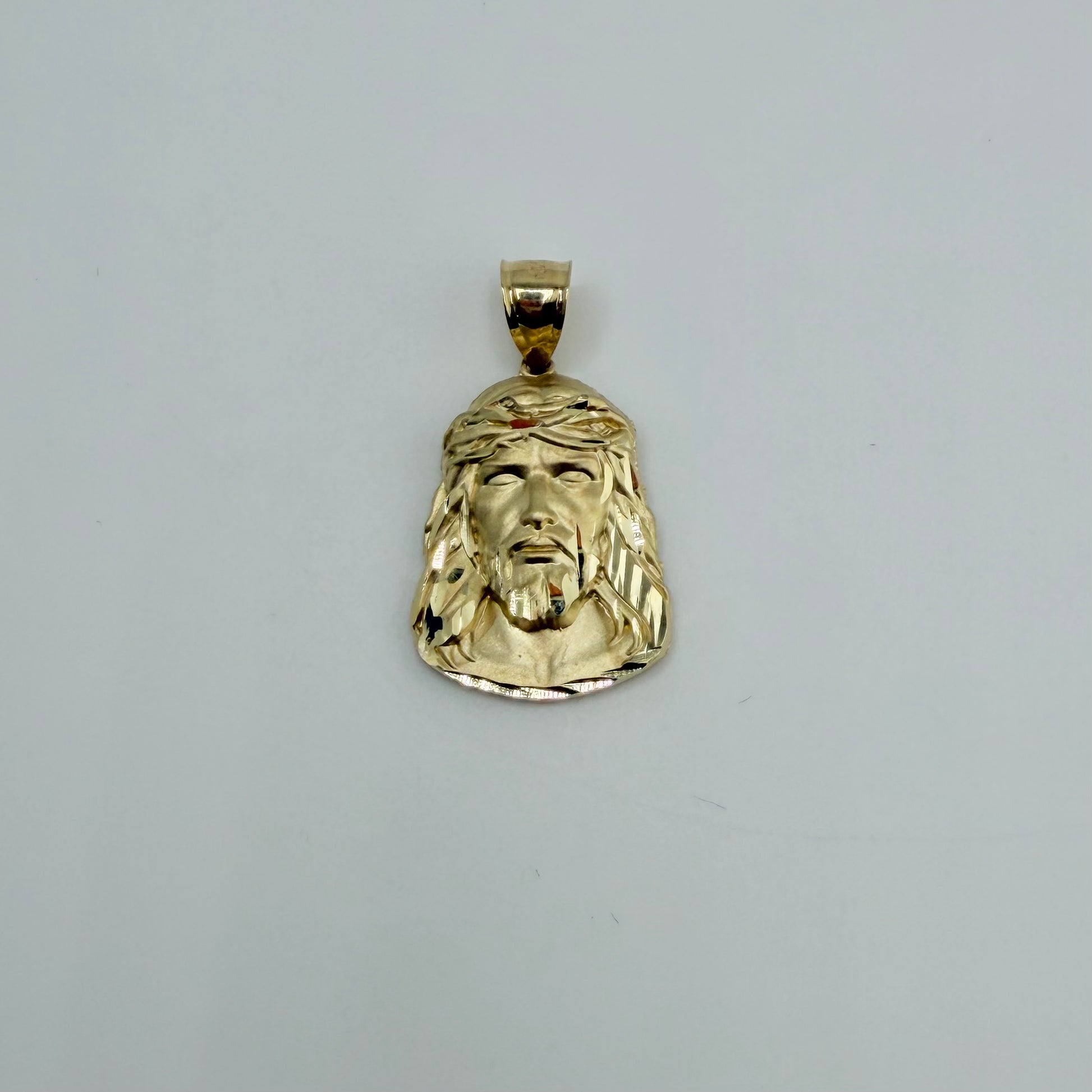Gold pendant with a face design on a gray background