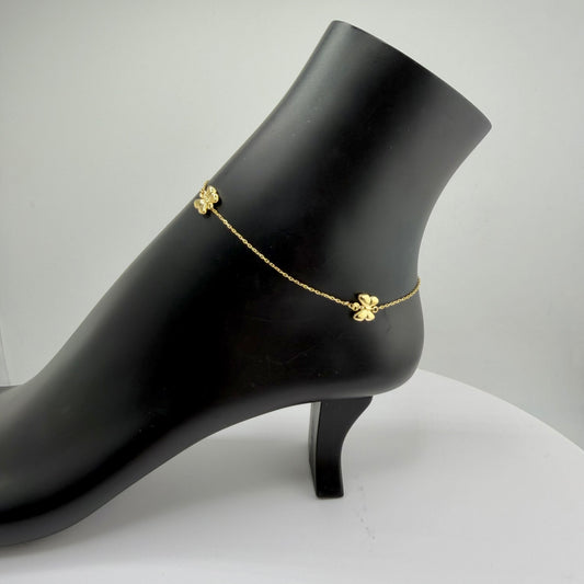 Gold anklet on a black high-heeled shoe against a gray background