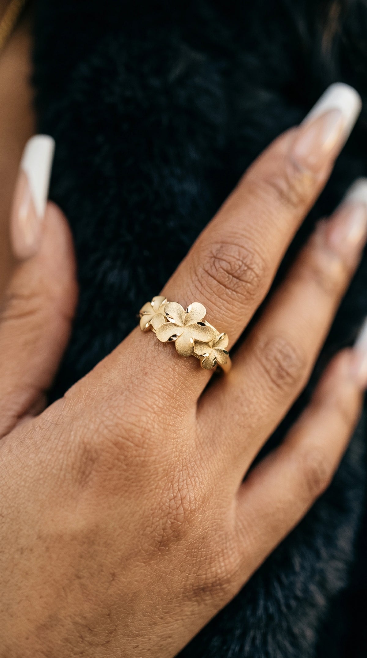 A close-up of a hand wearing a 14K Matte Finish Classic Hibiscus Ring, resting against a dark textured background.