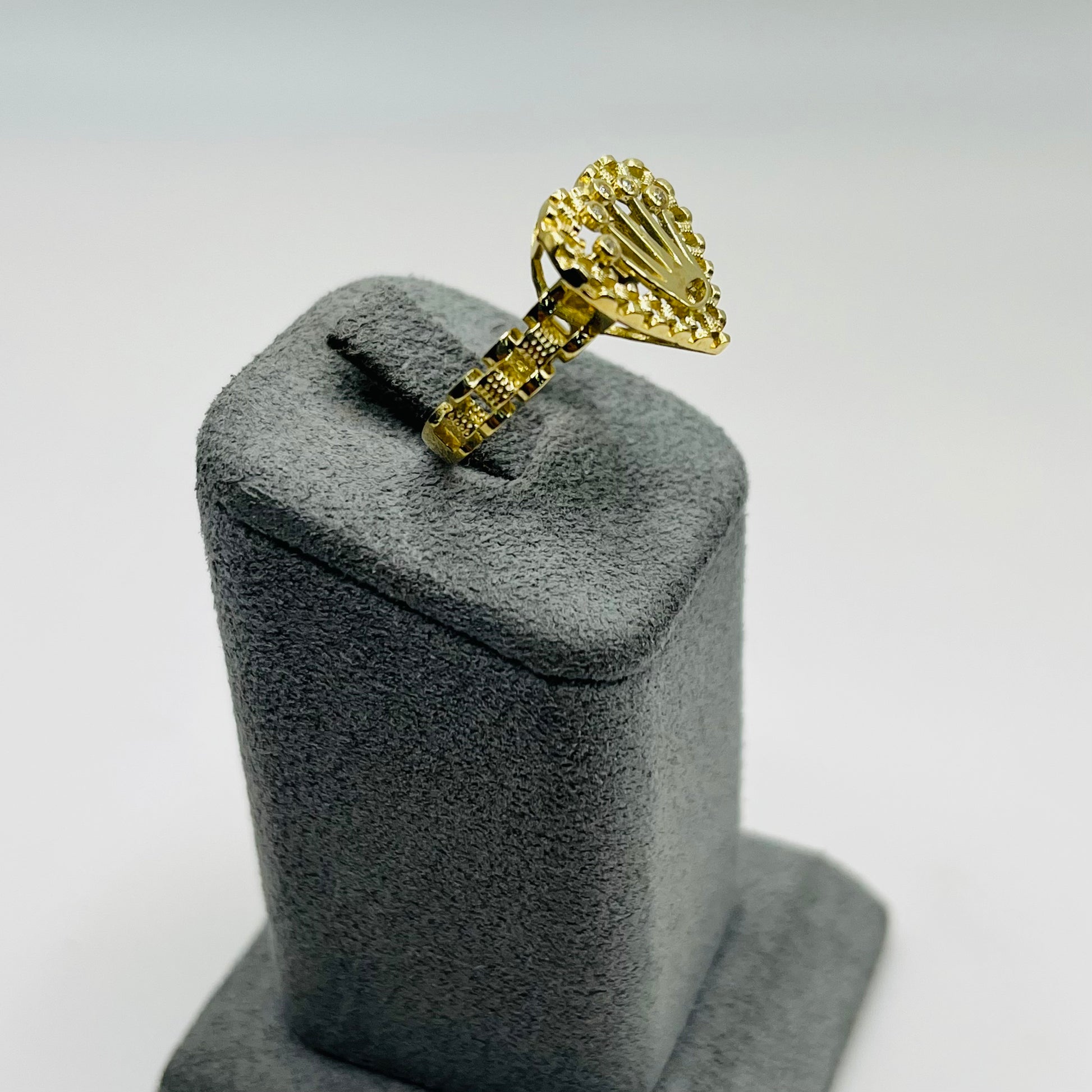 Gold ring with a unique design on a gray stand against a light gray background