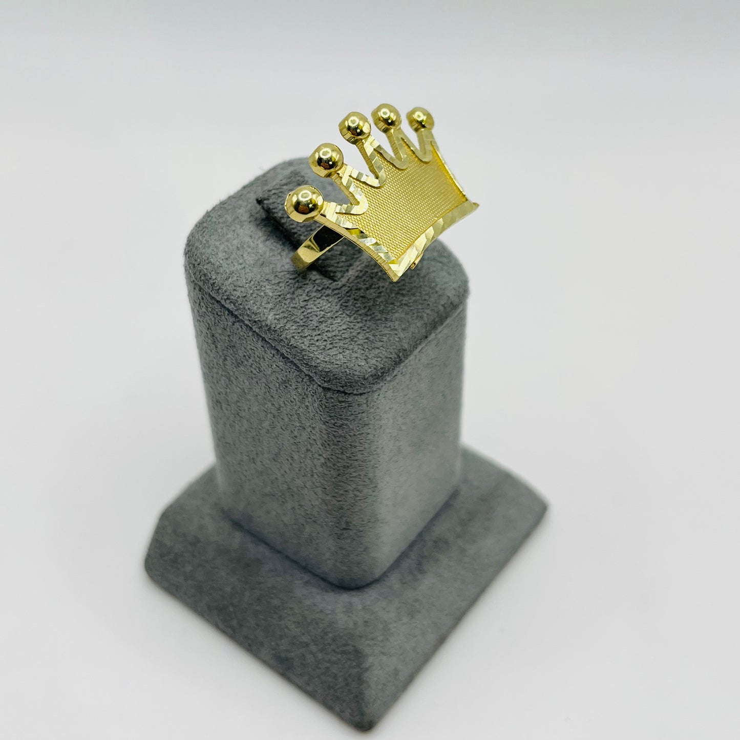 Gold ring with a crown design on a gray stand against a white background