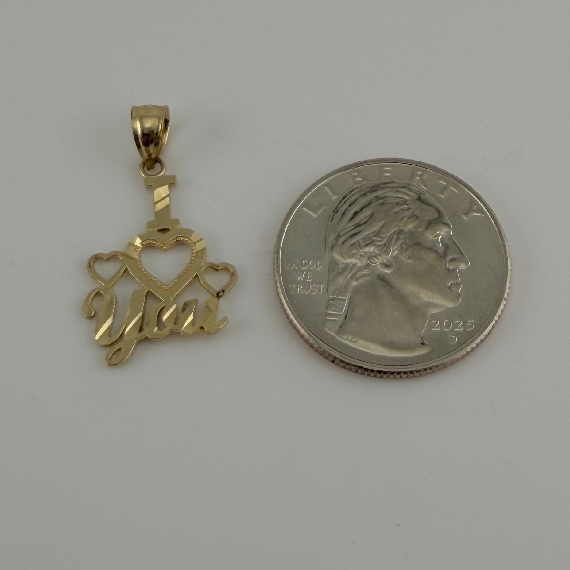 Gold pendant with 'Love' text next to a U.S. quarter on a gray background