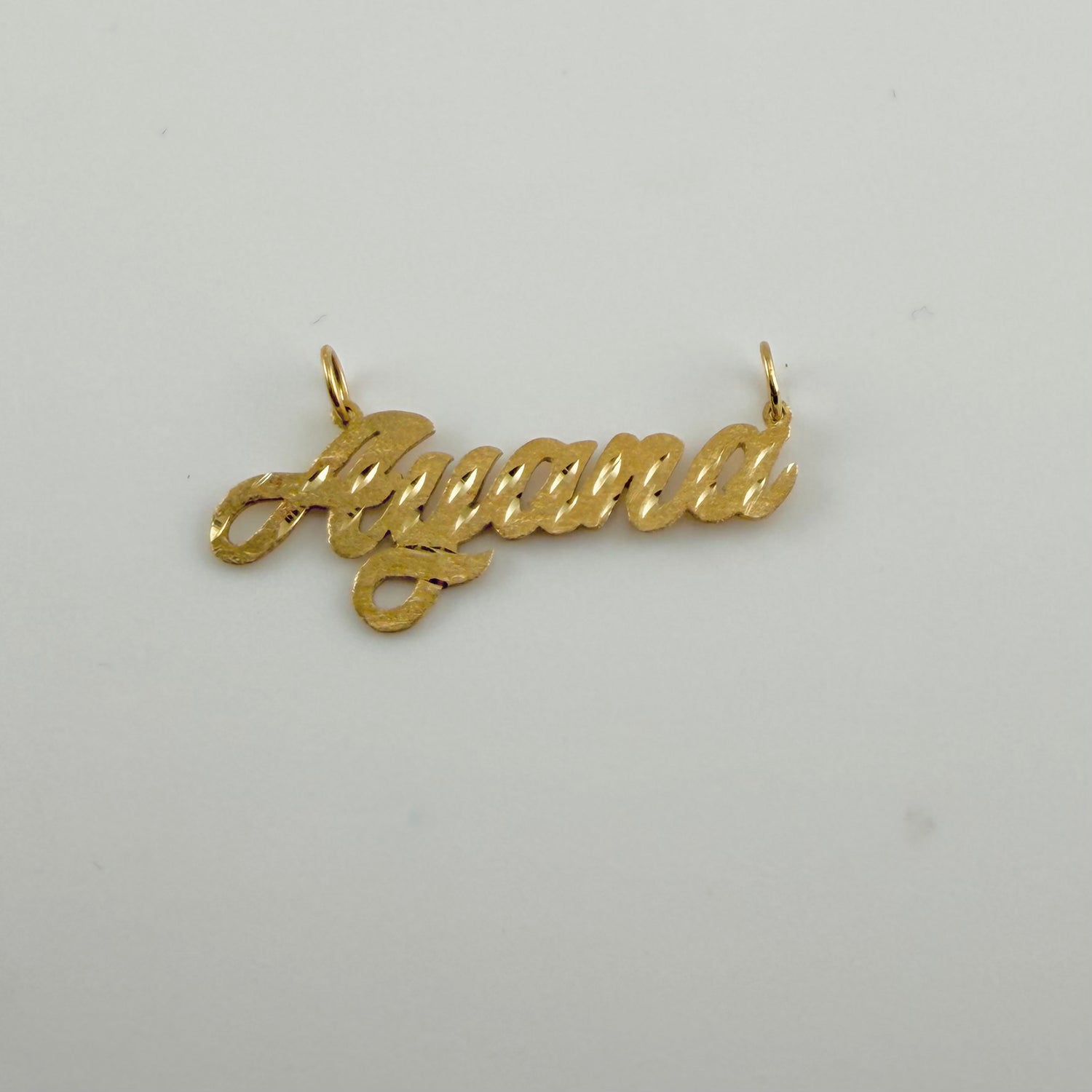 Gold pendant with 'Ayana' engraved on a light gray background