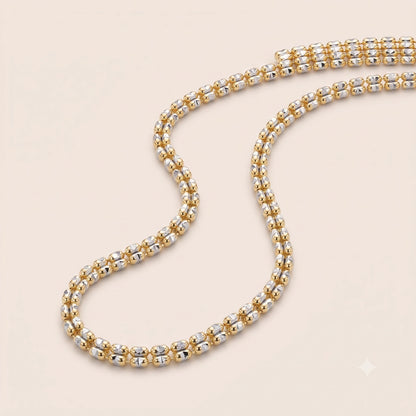 A 10K Gold 2.5MM Ice Chain featuring alternating yellow gold and white gold round beads, arranged in an S-shape on a light beige background.