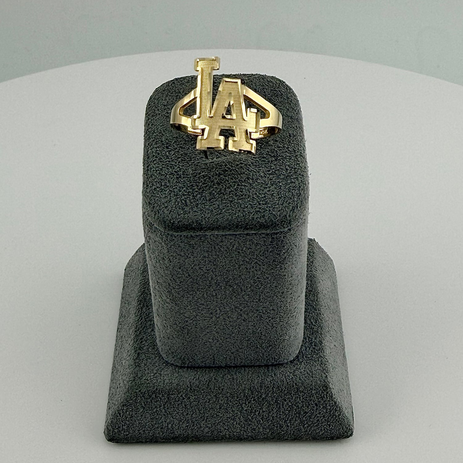 Gold ring with a logo on a gray stand against a light gray background