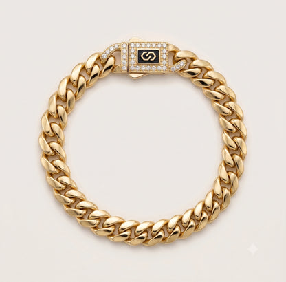 A 10K Gold Lightweight Monaco Bracelet with a diamond-encrusted clasp featuring a black center with a gold interlocking S logo, displayed on a light beige background.