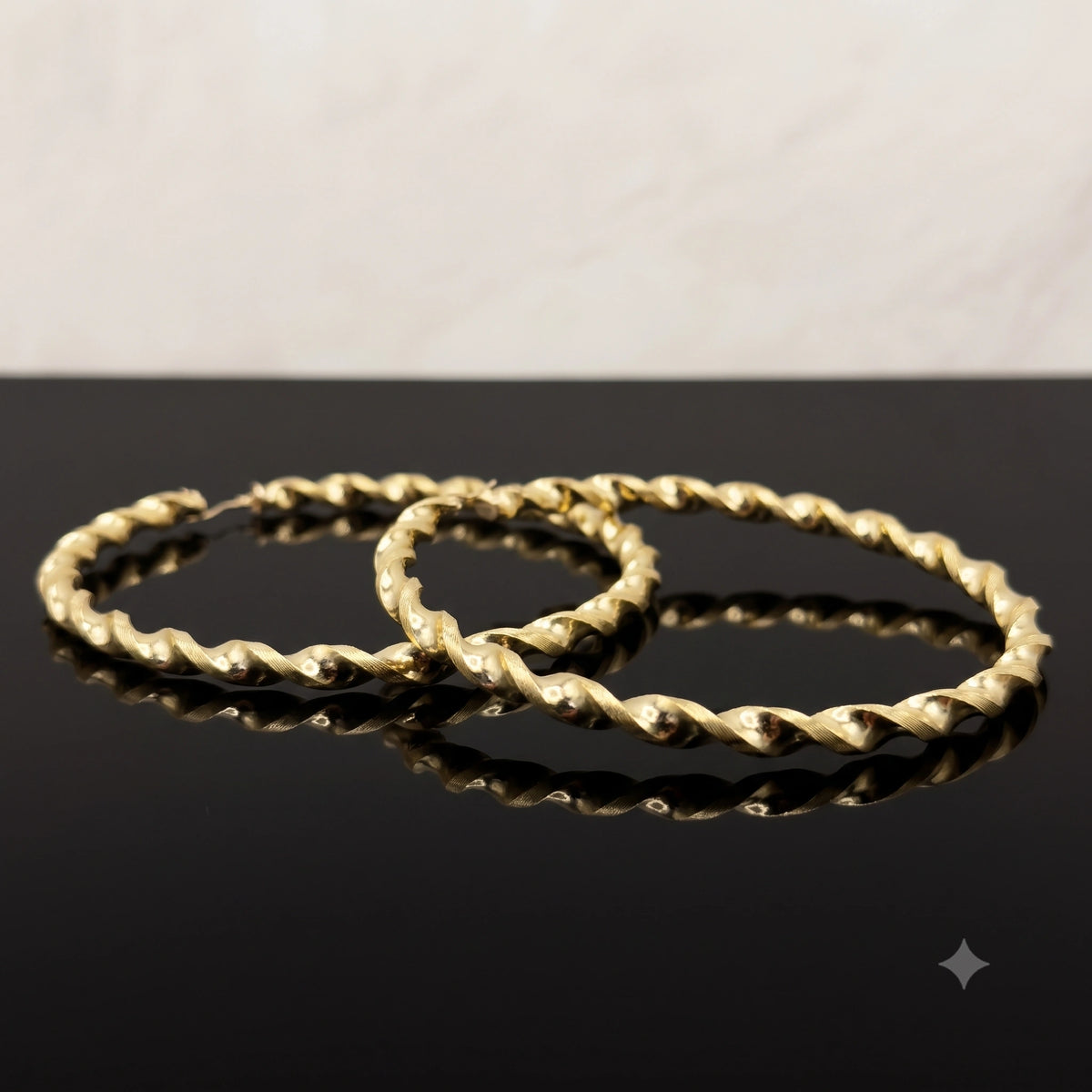 A pair of 10K Gold 4.3mm Twist Hoop Earrings displayed on a glossy black reflective surface against a light neutral background.